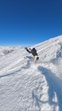 Person skiing down a snowy slope with a clear blue sky wearing Bluebird Ski suit
